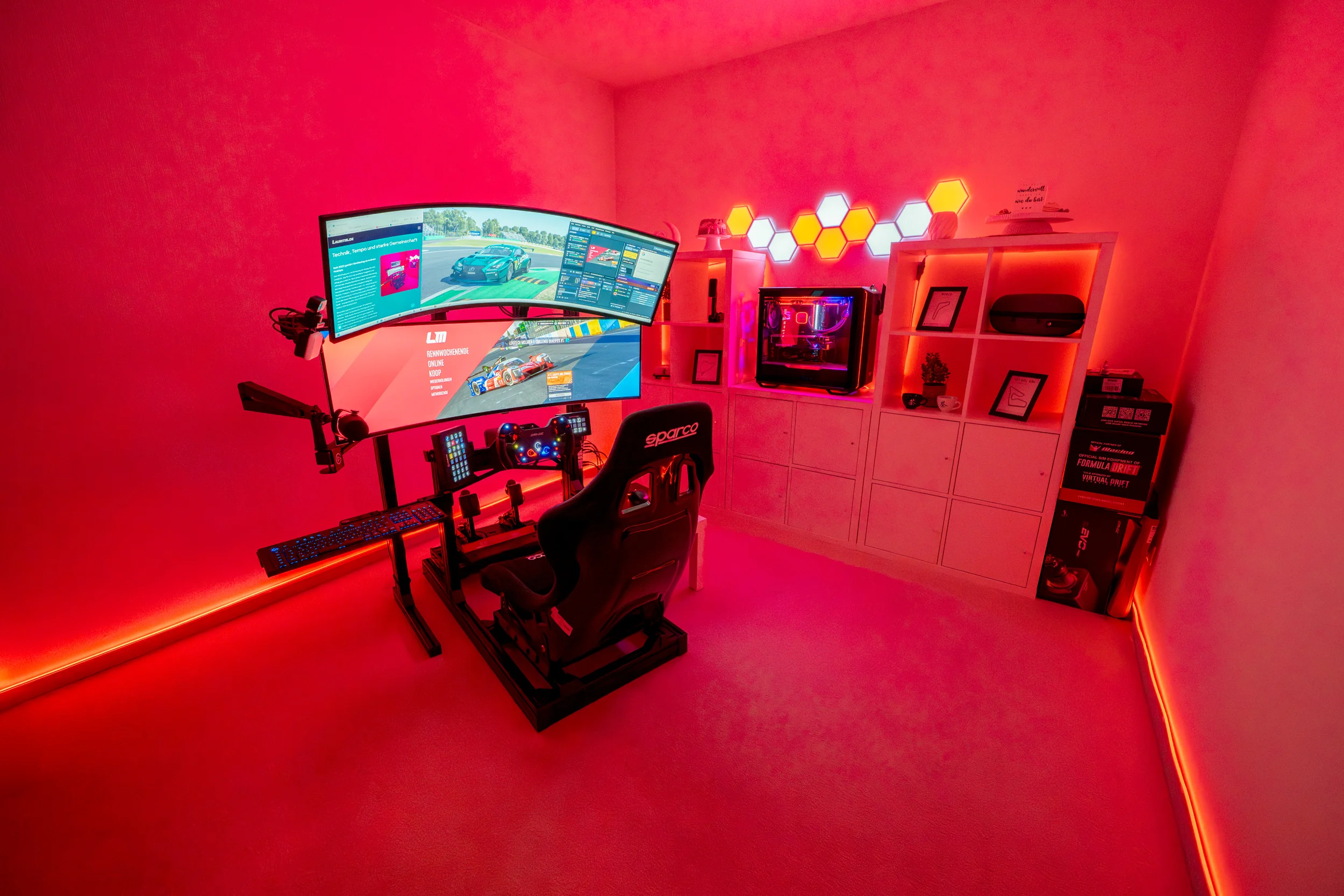 Red lit Gaming Room with a Curved Dual monitor Racing Setup Racing Chair and a White Shelf Unit with Hex Led Wall Accents Behind