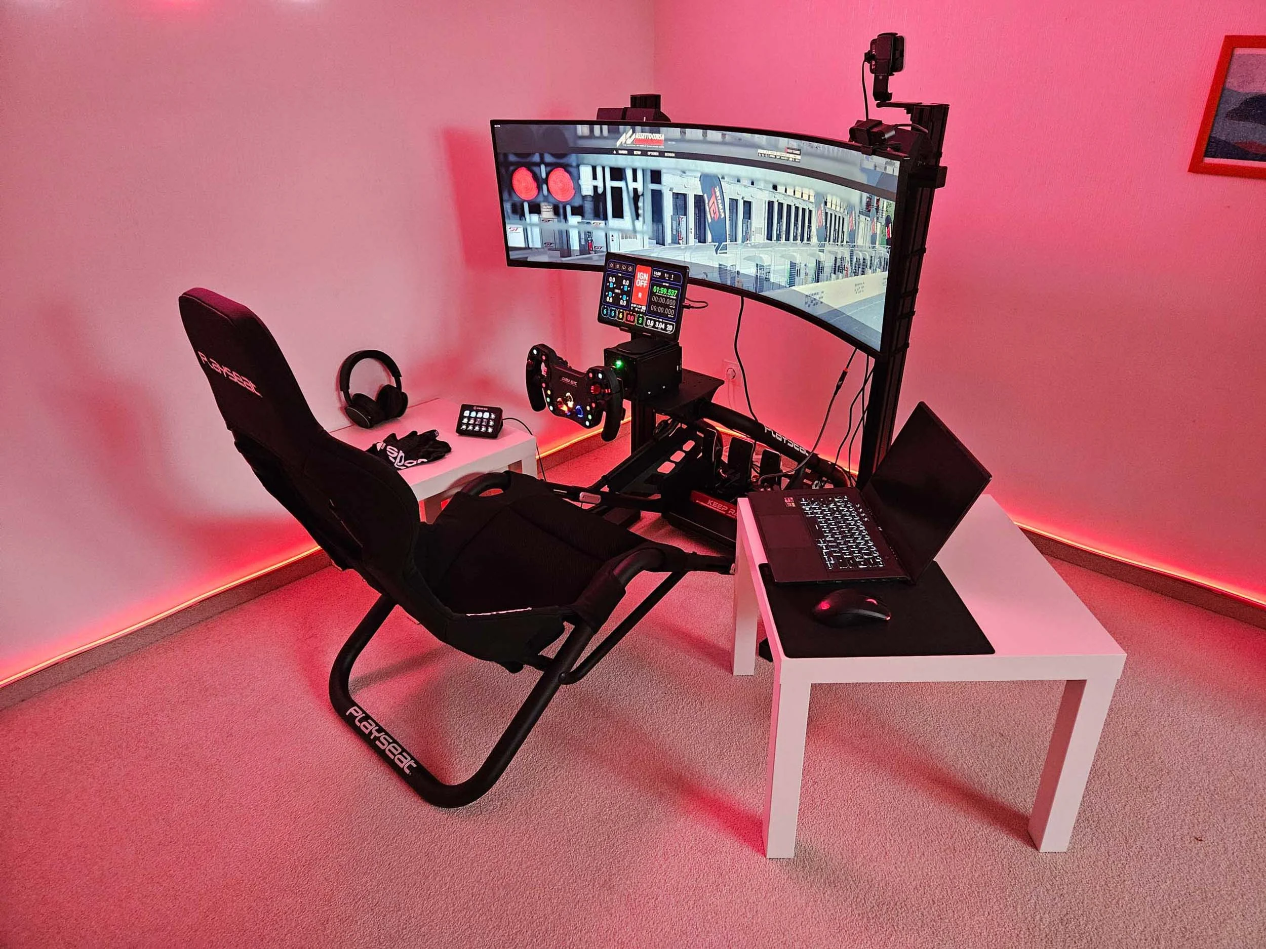 simracingpeterlauritisgt3simulation007 | Lauritisde Pink lit Racing Simulator Setup Featuring a Curved Monitor Steering Wheel with Pedals a Gaming Chair and a Laptop on a White Table