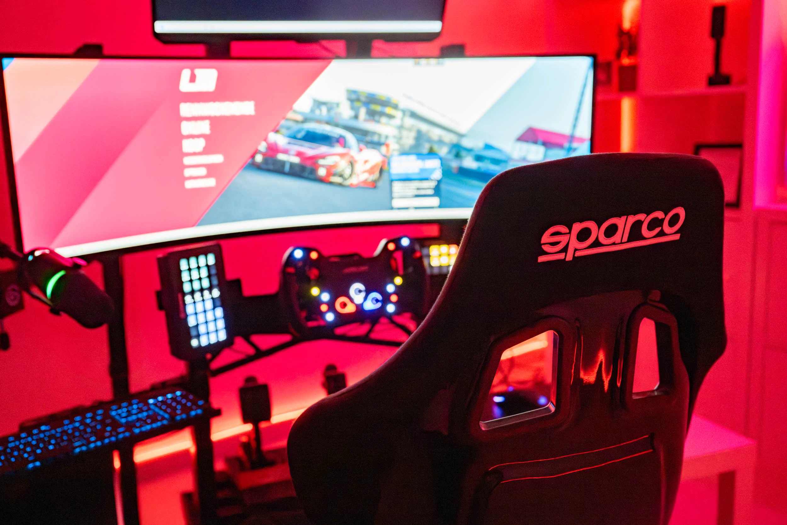 wwwpeterlauritisde | Lauritisde Gamer Setup with a Curved Monitor Showing a Racing Game and a Sparco Racing Chair in a Red lit Room